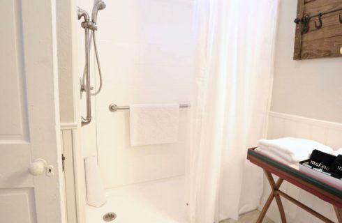 a bathroom with gray and white walls with a walk in shower, and black and white towels on a tray, along with a wooden board with hooks and a yellow hair dryer