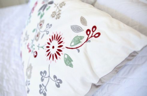 a colorful pillow with embroidered red, green, and grey flowers and leaves
