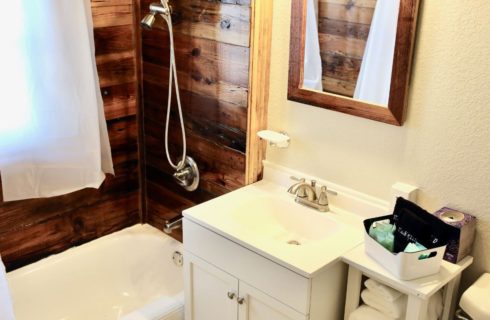 a bathroom with beige walls, a sink, sideboard with towels a tub and shower combination with dark knotty pine walls, and a mirror above the sink.